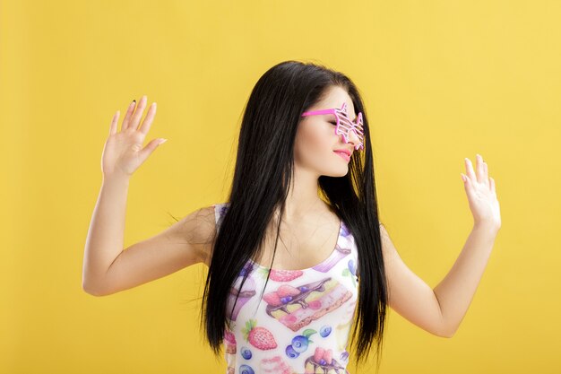 Atractiva joven morena en camiseta rosa sin mangas en amarillo mujer divertida con gafas de sol rosa bailando