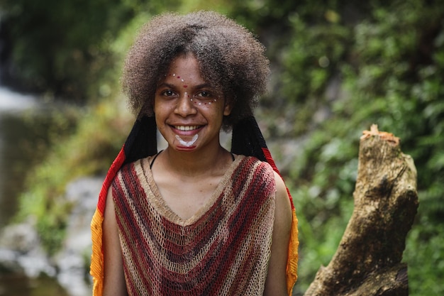 Atractiva joven papúa de la tribu dani con ropa tradicional está sonriendo contra la naturaleza backgro