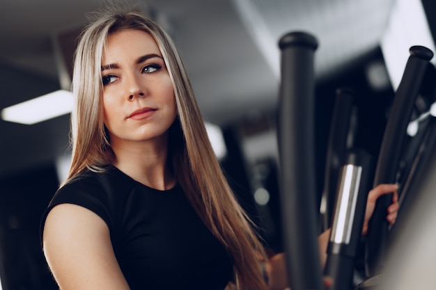 Atractiva joven rubia haciendo ejercicio en aparatos de entrenamiento cardiovascular