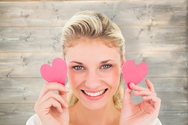 Atractiva joven rubia sosteniendo corazoncitos contra el fondo de tablones de madera blanqueada