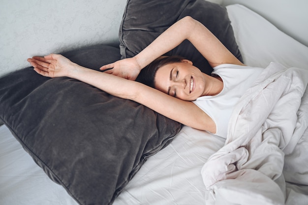 Atractiva joven sonriente que se extiende en la cama despertando solo, feliz concepto, despierto después de un sueño saludable en una cómoda cama cómoda y un colchón disfrutan de buenos días