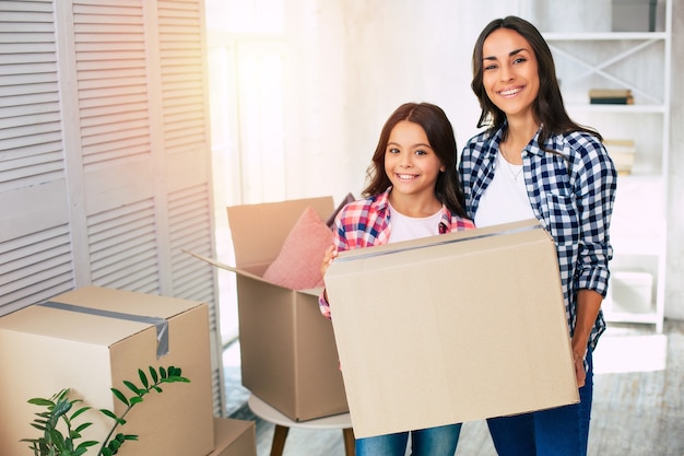 Atractiva joven y su hijo sostienen cajas de cartón en su nueva casa después de la reubicación