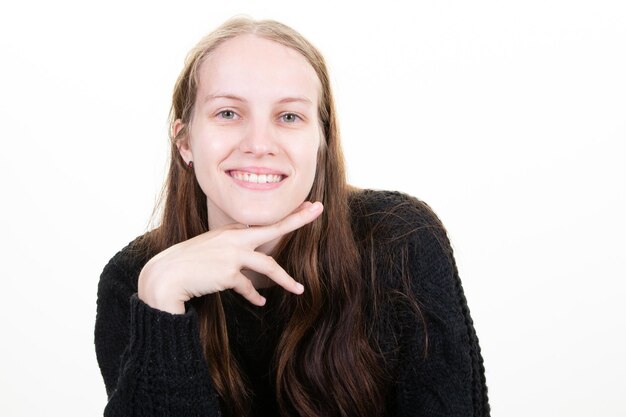 Atractiva linda rubia sonriente mujer joven de pie mano bajo la barbilla feliz y sonrisa en fondo blanco.