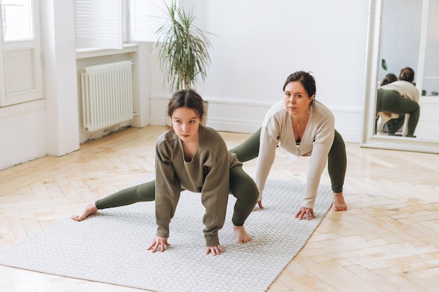 Atractiva madre mujer de mediana edad e hija adolescente practican yoga juntos en la habitación luminosa