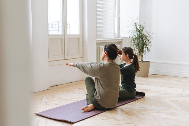 Atractiva madre mujer de mediana edad e hija adolescente practican yoga juntos en la habitación luminosa