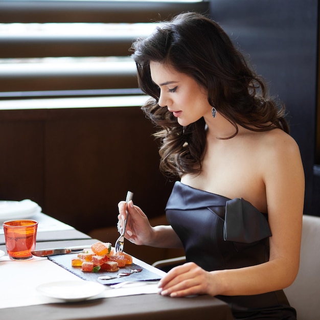 Atractiva modelo femenina con cabello arreglado y maquillaje con un vestido elegante que sirve postre en el restaurante