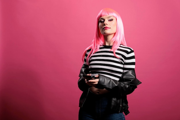 Atractiva modelo femenina con smartphone y chaqueta de cuero sentada sobre el fondo del estudio, sintiéndose segura y divertida con un estilo rockero moderno. Vistiendo sensuales artículos de moda sexy y punk.