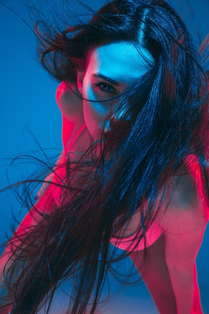 Atractiva modelo morena sobre fondo azul de estudio en luz de neón