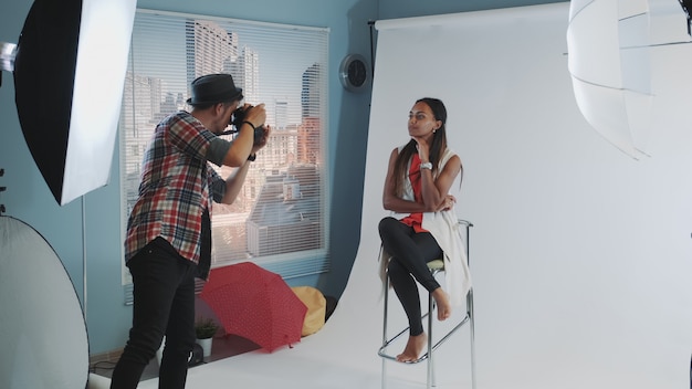 Foto atractiva modelo de raza mixta posando en una silla alta de bar para una sesión de fotos en una revista de moda.