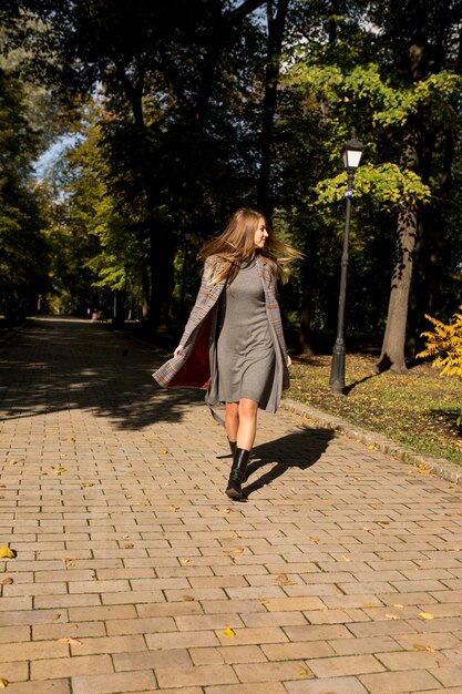 Atractiva modelo rubia con pelo largo en vestido de punto y abrigo caminando en el parque en un día soleado