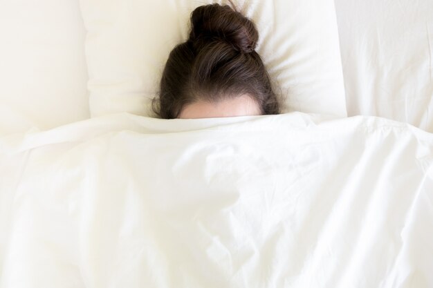 Atractiva morena joven debajo de la manta en la cama a la hora de la mañana