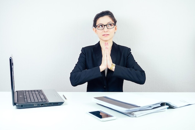 Atractiva morena multitarea mujer de negocios con elegantes gafas de traje de negocios que trabaja con una computadora portátil y un montón de carpetas practica yoga y se relaja en el concepto de negocio de oficina y la fecha límite