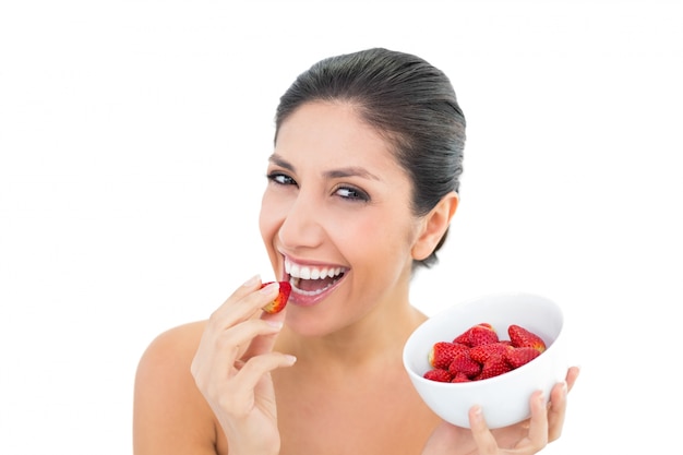Atractiva morena sosteniendo un plato de fresas frescas y comiendo uno