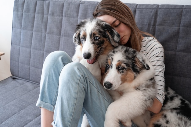 Atractiva mujer abrazando, besando a dos lindo cachorro de merle azul pastor australiano.