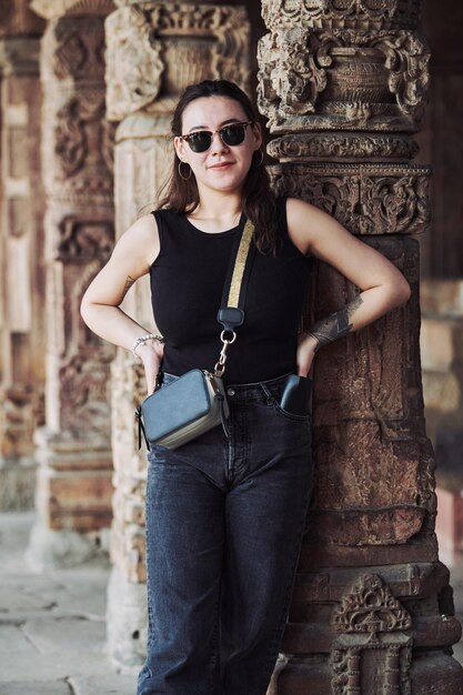 Atractiva mujer del este de Asia con gafas de sol negras y ropa negra se encuentra entre pilares antiguos