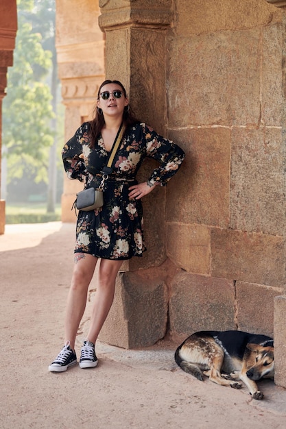 Atractiva mujer del este de Asia vestida con gafas de sol negras se encuentra cerca de un perro acostado en una antigua tumba india