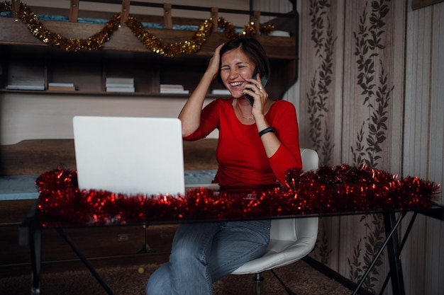 Atractiva mujer asiática con caja de regalo tomando una llamada contra una acogedora habitación decorada