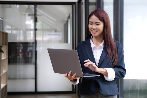 Atractiva mujer asiática joven que usa una computadora portátil mientras está de pie en una oficina