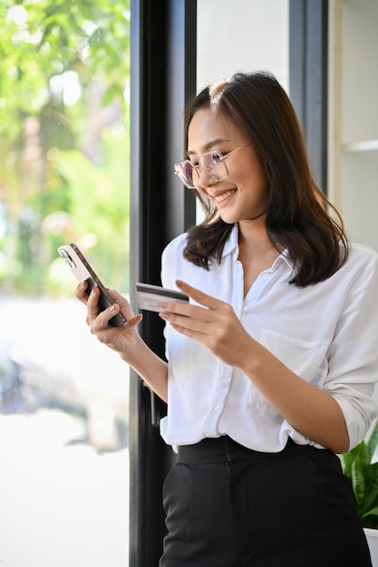 Atractiva mujer asiática pagando sus facturas mediante una aplicación de pago de banca móvil