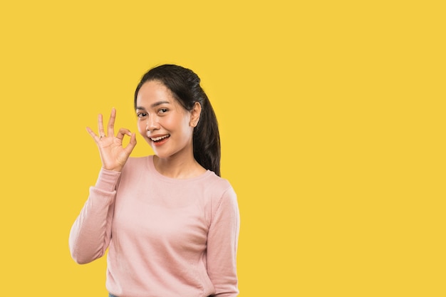 Atractiva mujer asiática sonriendo con gesto de la mano bien mientras mira a la cámara