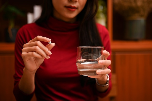 Atractiva mujer asiática sosteniendo un vaso de agua y una tableta de medicina imagen recortada