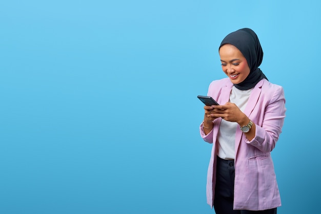 Atractiva mujer asiática mediante teléfono móvil con espacio vacío sobre fondo azul.