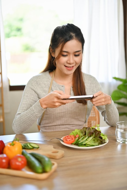 Atractiva mujer asiática tomando una foto de su ensalada casera con su teléfono inteligente