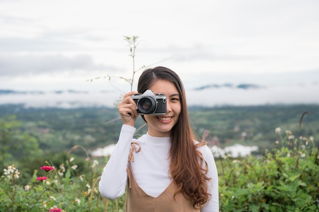 Atractiva mujer asiática tomando fotos con cámara de película retro entre la naturaleza en el campo por la mañana