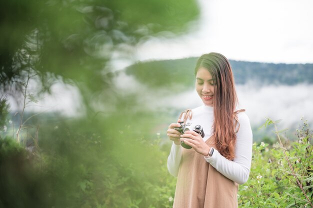 Atractiva mujer asiática tomando fotos con cámara de película retro entre la naturaleza en el campo por la mañana