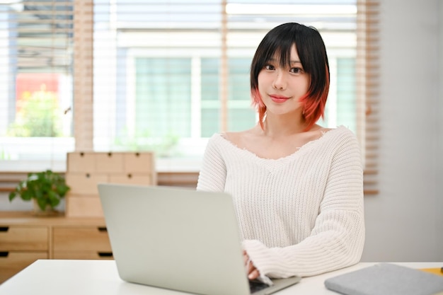 Atractiva mujer asiática usando su computadora portátil en su espacio de trabajo en casa