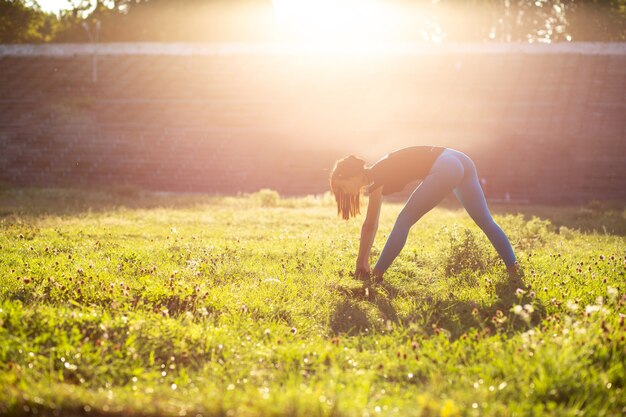 Atractiva mujer atlética que se extiende antes del entrenamiento en el estadio. Tiro al aire libre con rayos de sol. Espacio para texto