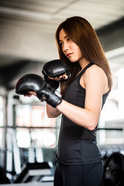 Atractiva mujer boxeadora entrenando con kick boxing en el gimnasio con guantes negros.