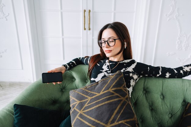 Atractiva mujer caucásica en auriculares relajándose en un cómodo sofá en casa y escuchando música.