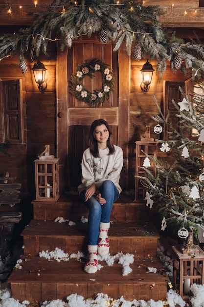 Atractiva mujer caucásica con cabello oscuro cerca del árbol de Navidad decorado en ambiente de año nuevo