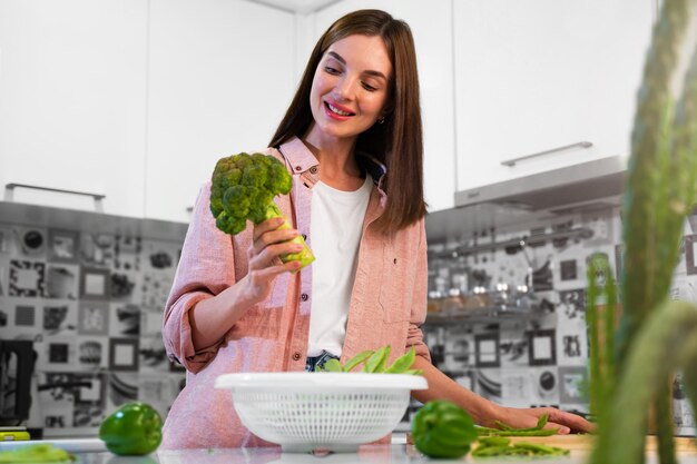 Atractiva mujer caucásica cocinará ensalada verde en la cocina de su casa. Hermosa chica que se siente feliz y disfruta comiendo verduras, alimentos saludables que se usan para desintoxicar la dieta y perder peso para el cuidado personal y la salud.