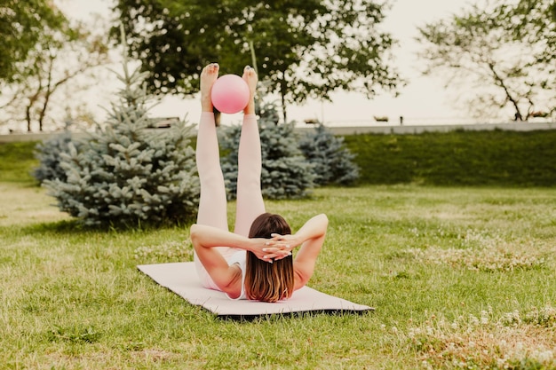 Atractiva mujer caucásica hacer pilates con pelota y hacer ejercicio entrecruzado en la hierba verde del césped al atardecer