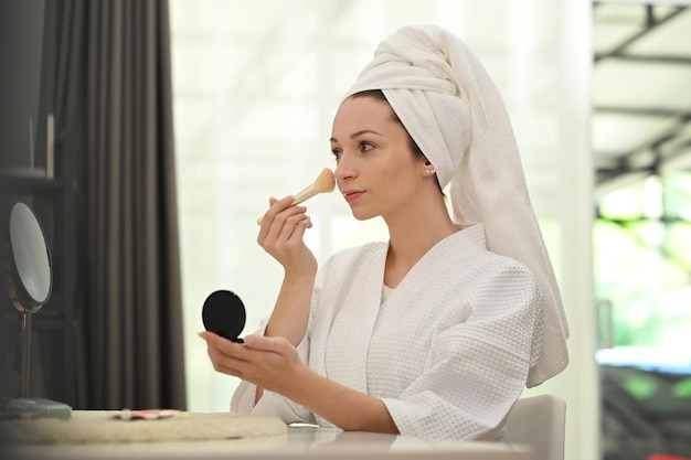 Atractiva mujer caucásica haciendo maquillaje diario y aplicando polvo de rubor en las mejillas Concepto de cuidado de la belleza y cosméticos