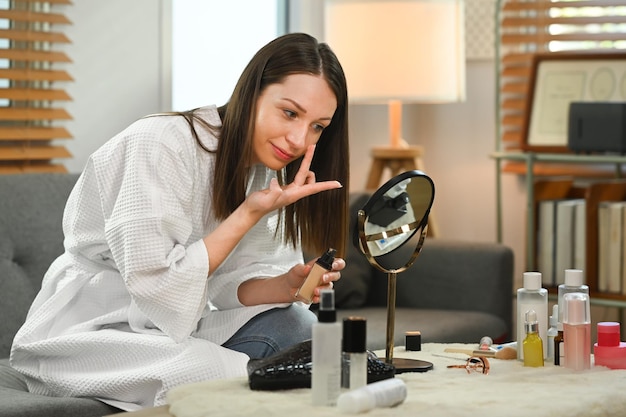 Atractiva mujer caucásica mirándose al espejo y aplicando base en su rostro Concepto de belleza y cosmética