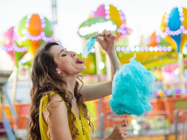 Atractiva mujer caucásica posando con algodón de azúcar azul en un carnaval