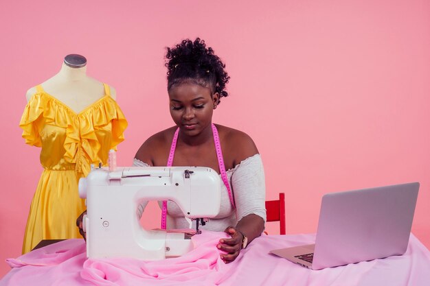 Atractiva mujer costurera junto al maniquí con máquina de coser sobre fondo rosa en el estudio copyspace. concepto de idea e inspiración.