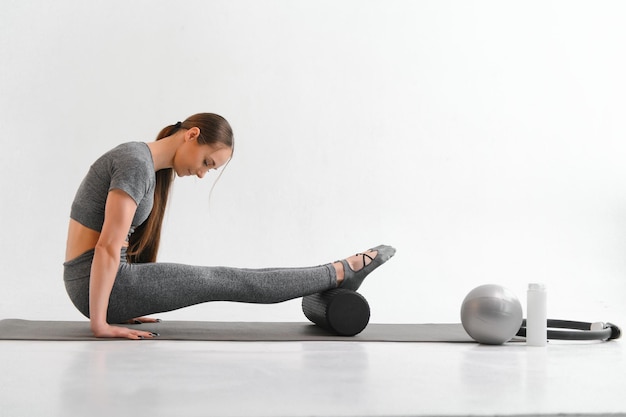 Atractiva mujer delgada haciendo ejercicios de estiramiento en una alfombra negra en un moderno y brillante gimnasio