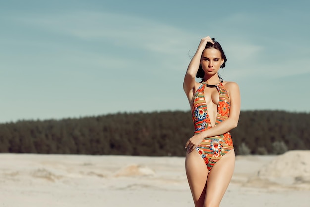 Atractiva mujer delgada en traje de baño ornamental mirando hacia otro lado en el fondo borroso de la playa y el cielo en el día de verano