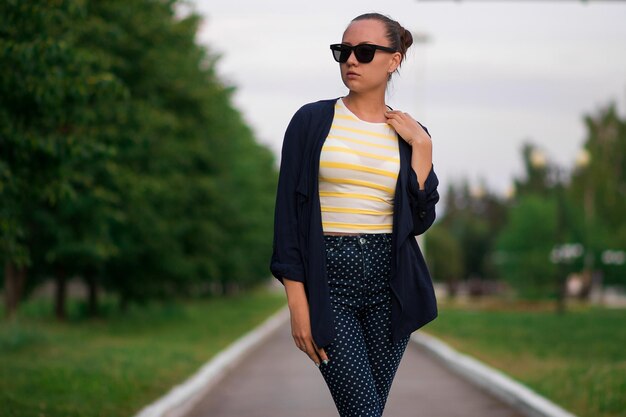 Atractiva mujer delgada y tranquila con camisa a rayas amarillas y blancas y azul con pantalones de lunares blancos