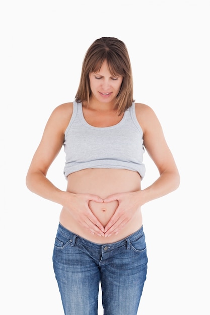 Atractiva mujer embarazada posando mientras forma un corazón con sus manos