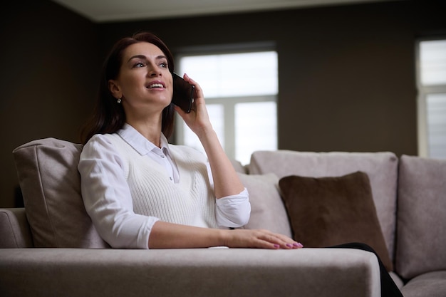 Atractiva mujer europea hablando por teléfono móvil sentada en un cómodo sofá de terciopelo