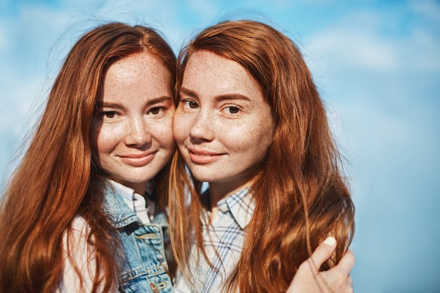 Atractiva mujer feliz con cabello rojo y pecas, abrazándose y sonriendo, mirando felizmente, estando en una relación cercana, confiando y amándose.