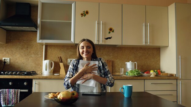 Atractiva mujer feliz recibe buenas noticias leyendo una carta en la cocina mientras desayuna