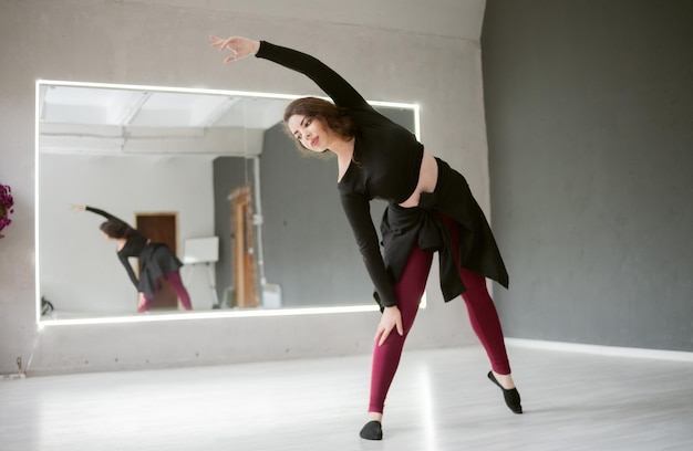 Atractiva mujer gimnasta o bailarina haciendo ejercicios de gimnasia en el interior en el estudio de danza