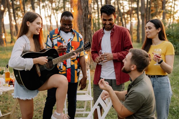 Atractiva mujer hipster tocando la guitarra ganando a los hombres en una cena con amigos multirraciales