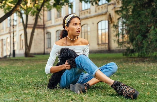 atractiva mujer hispana sentada con un perro en el césped del parque y relajándose el fin de semana